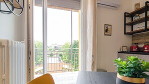 Un comedor con una mesa, sillas, una planta en maceta y vistas a un balcón con barandilla y vegetación.