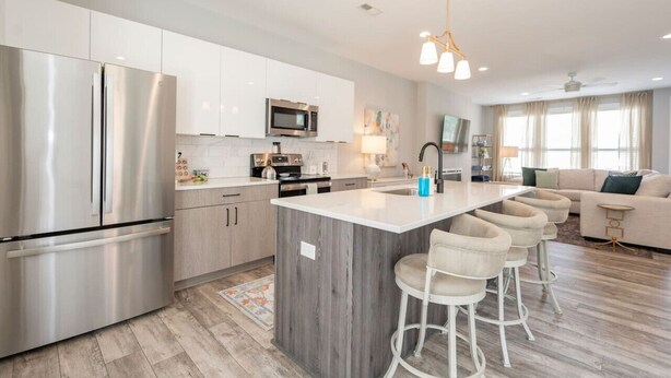 Una cocina moderna con electrodomésticos de acero inoxidable, una isla central con taburetes de bar y una zona de comedor con sofá y televisor.