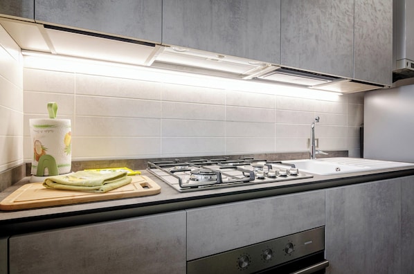 A modern kitchen with a gas stove, a sink, and a wooden cutting board with a green towel.