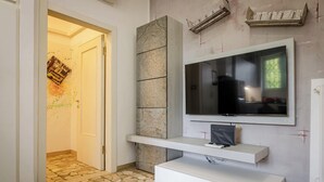 Un salon moderne doté d’un grand téléviseur à écran plat fixé sur un mur en pierre, d’un meuble de rangement blanc en dessous et d’un sol carrelé à motifs.