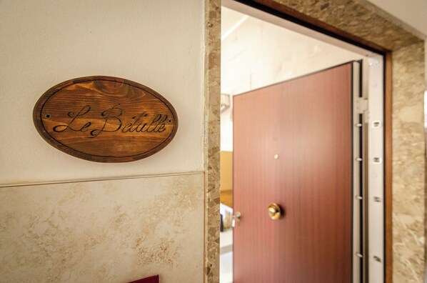 Une enseigne en bois portant l’inscription « Le Betule » est fixée à un mur, une porte fermée avec une poignée en laiton, et un mur de pierres.