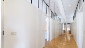 A modern hallway with glass partitions, wooden flooring, and a ceiling with recessed lighting.