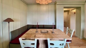 A dining area with a wooden table, white chairs, and a bench. There is a lamp on the left and a chandelier above the table. - Cozy 2 bedroom flat with beautiful views (Cortina d'Ampezzo)