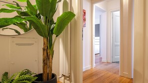 Een gang met een potplant, houten vloer en witte wanden.