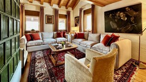 A cozy living room with a wooden ceiling, two sofas with red cushions, a coffee table, and a large painting on the wall. - Classy 3 bedroom few steps from centre (Cortina d'Ampezzo)