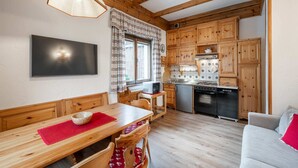 A cozy kitchen with wooden cabinets, a dining table with chairs, and a modern TV.