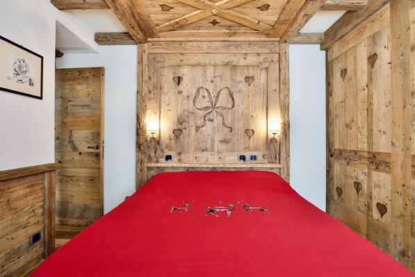 Una habitación con techo de madera, una cama con colcha roja y una pared con recortes en forma de corazón y un gran lazo decorativo.