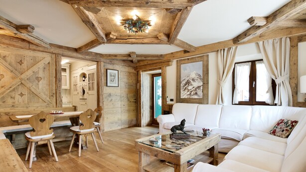 Ein rustikaler Innenraum mit Holzbalken, einem weißen Sofa, Holzstühlen und einem Glastisch.