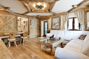 Un interior rústico con vigas de madera, un sofá blanco, sillas de madera y una mesa de centro de vidrio.