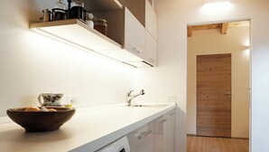Una cocina moderna con armarios blancos, un lavamanos de acero inoxidable y una puerta de madera al fondo.