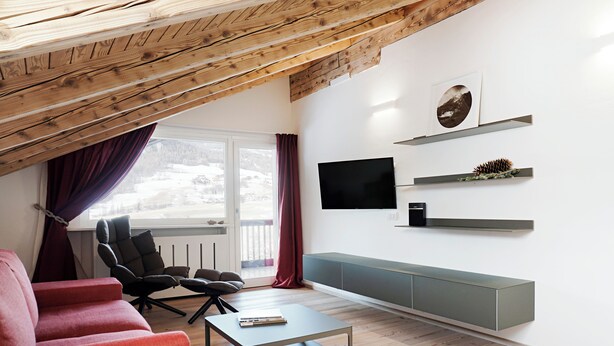 Una sala de estar moderna con techo inclinado, un ventanal con cortinas, un televisor de pantalla plana montado en la pared y un banco empotrado a lo largo de la pared.