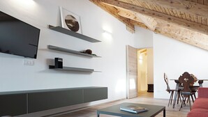 Una sala moderna con televisor de pantalla plana, estanterías empotradas, zona de comedor con mesa y sillas de madera, y sofá rojo.