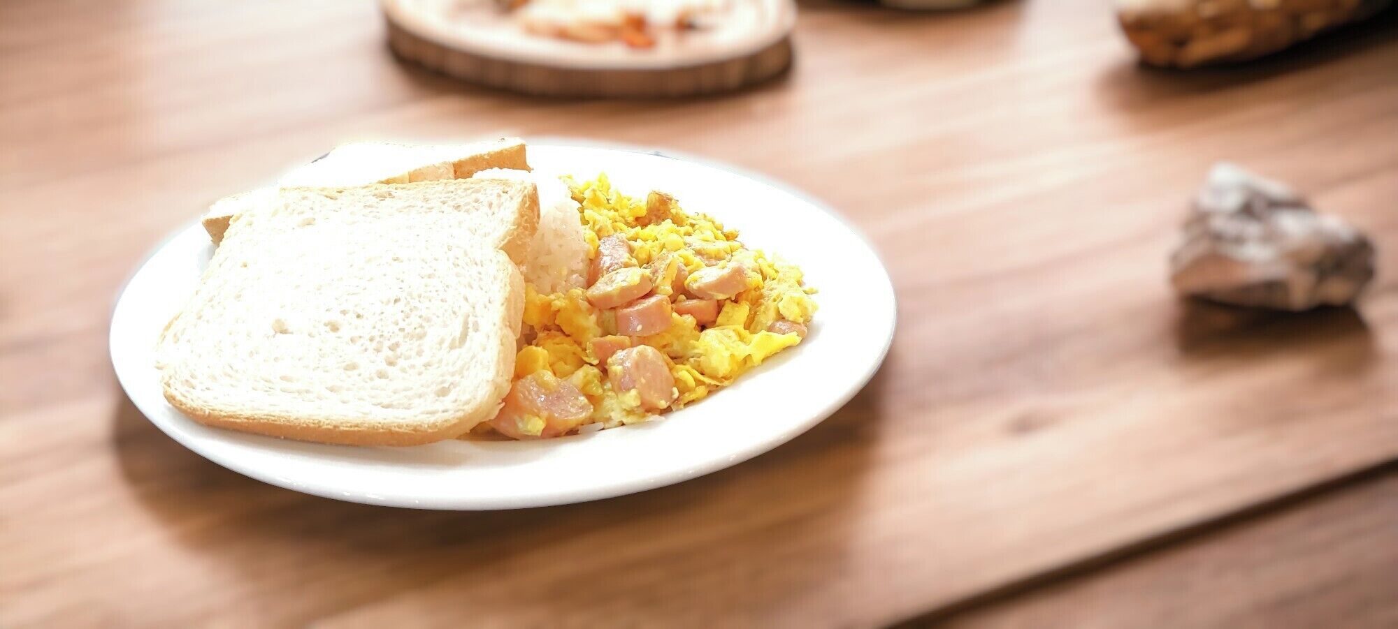 A plate with scrambled eggs and sausage on a wooden table.