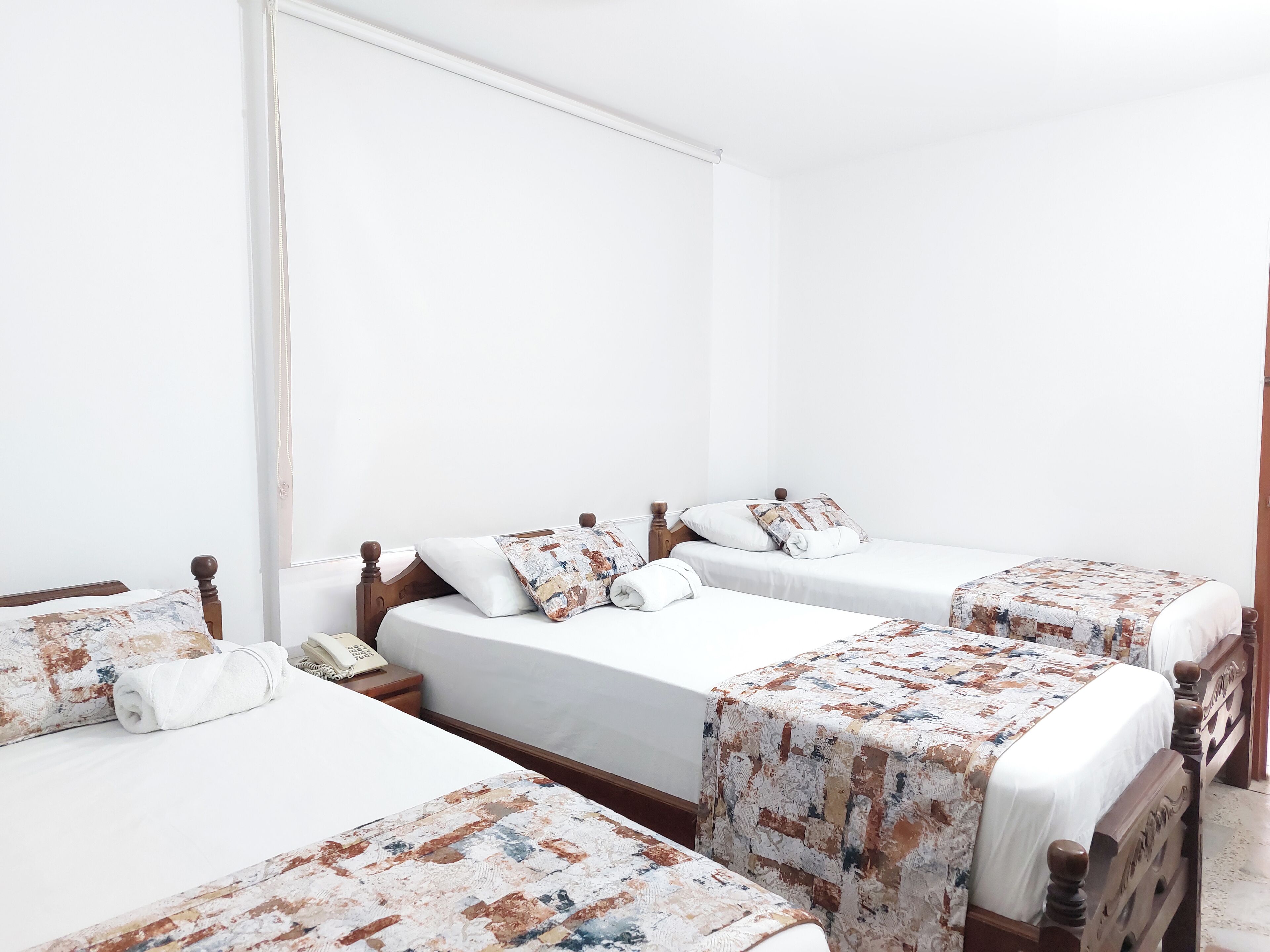 A hotel room with four single beds, each with a wooden headboard and white bedding.