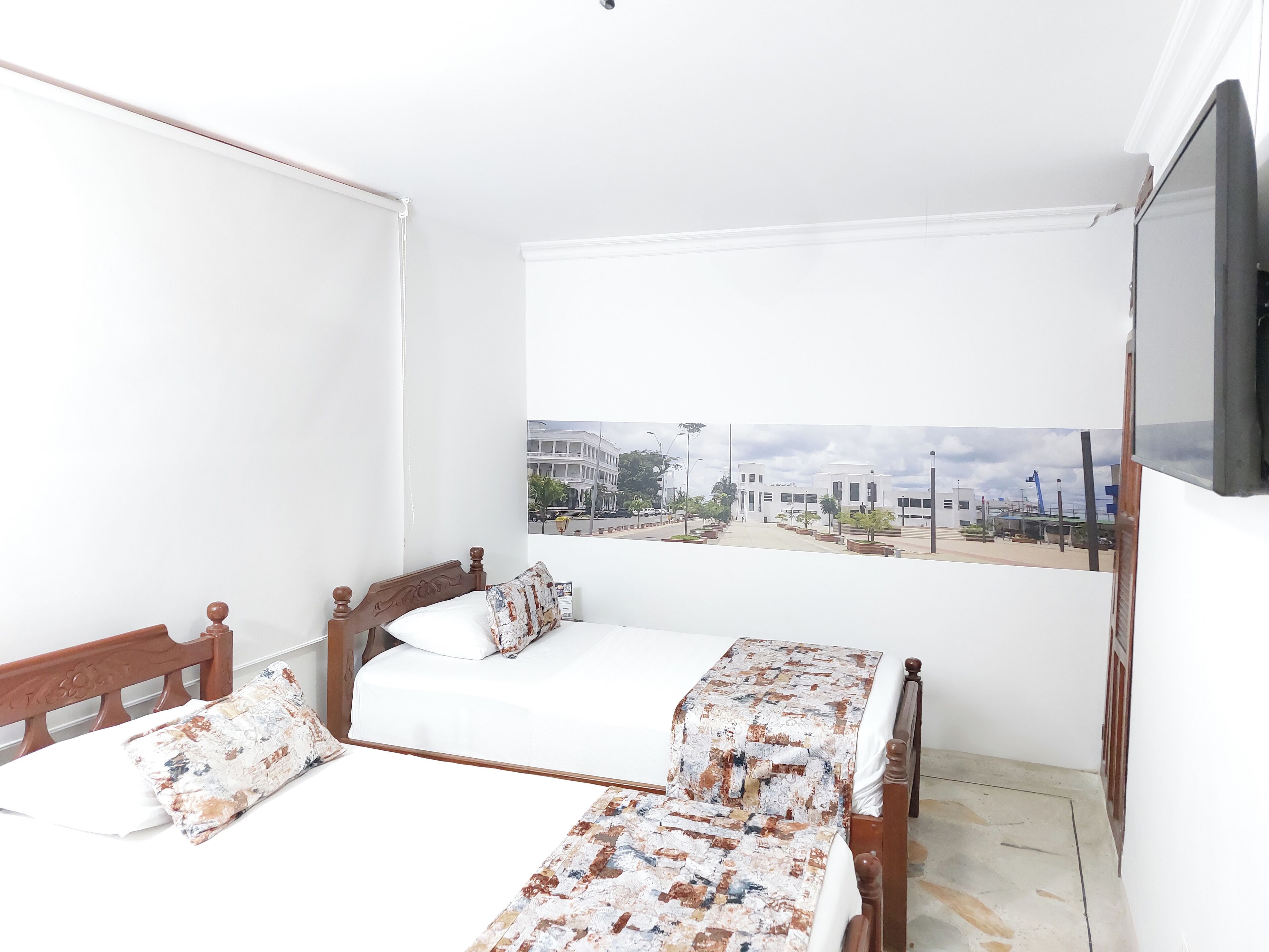 A bedroom with two wooden beds, white bedding, and a view of a cityscape through a window.