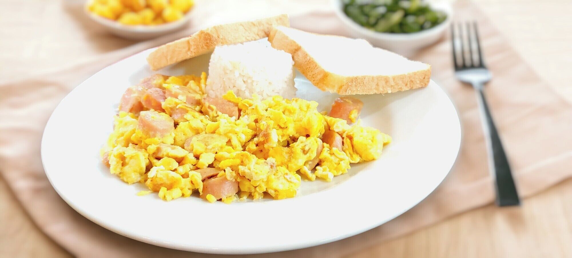 A plate of scrambled eggs with ham and toast on a white plate.
