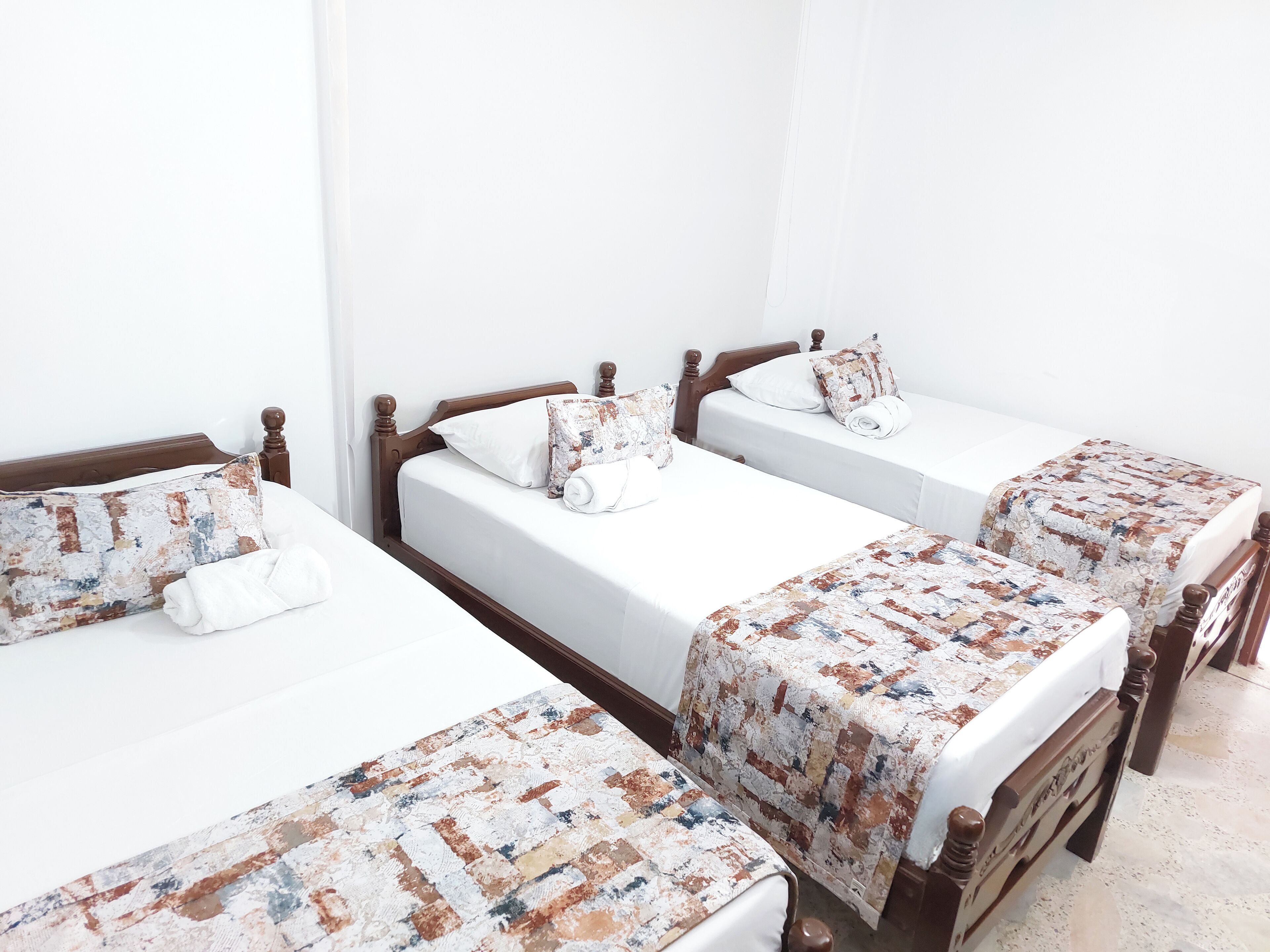 A hotel room with three wooden beds, each with a white mattress and a patterned blanket.