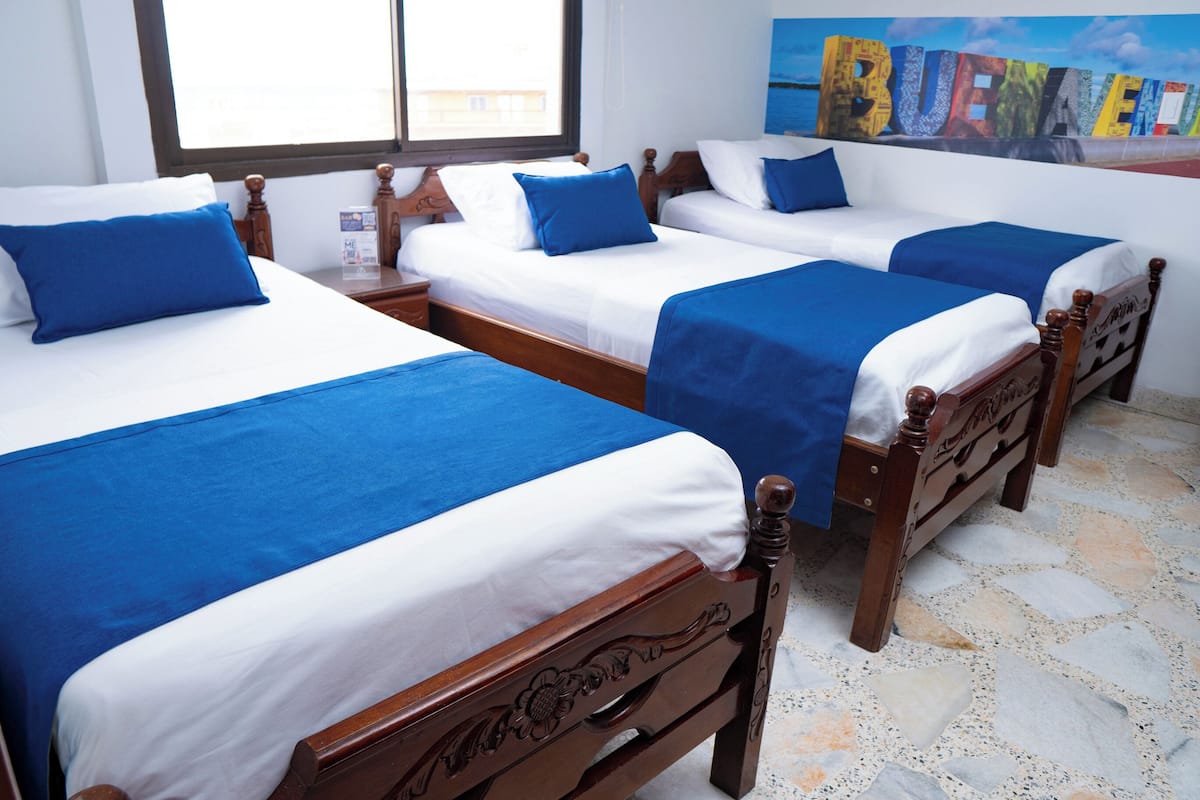 Une chambre d’hôtel avec trois lits en bois, chacun agrémenté de draps blancs et bleus.