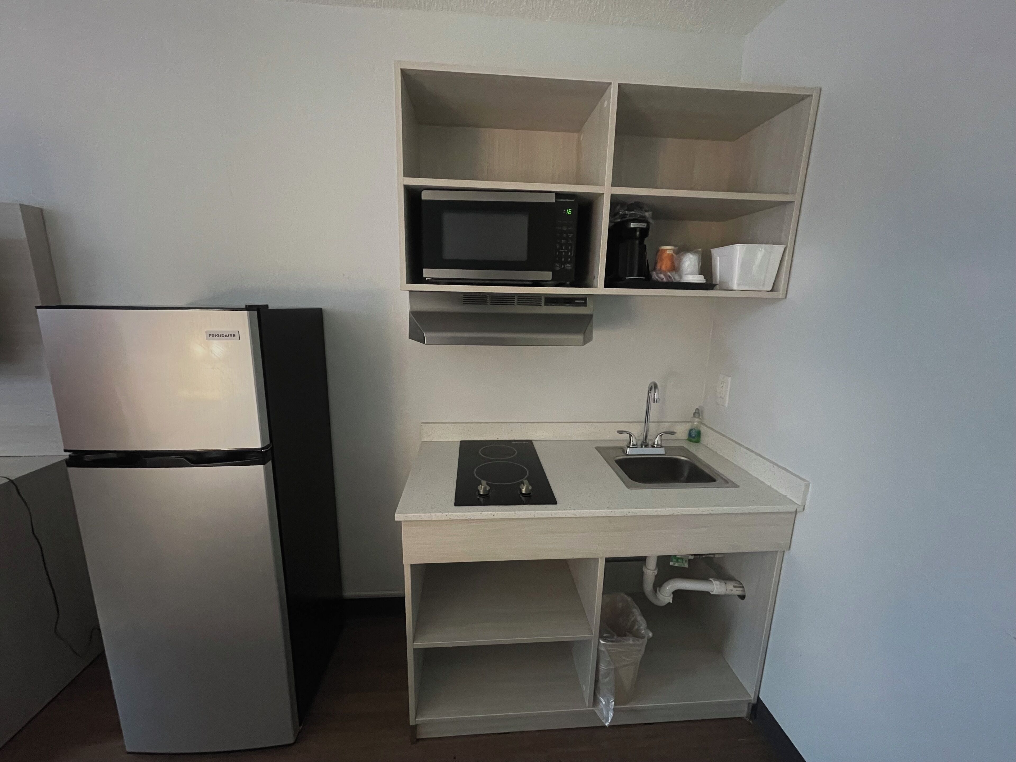 A compact kitchenette with a refrigerator, microwave, sink, and a small countertop.