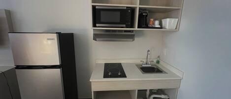 A compact kitchenette with a refrigerator, microwave, sink, and a small countertop.