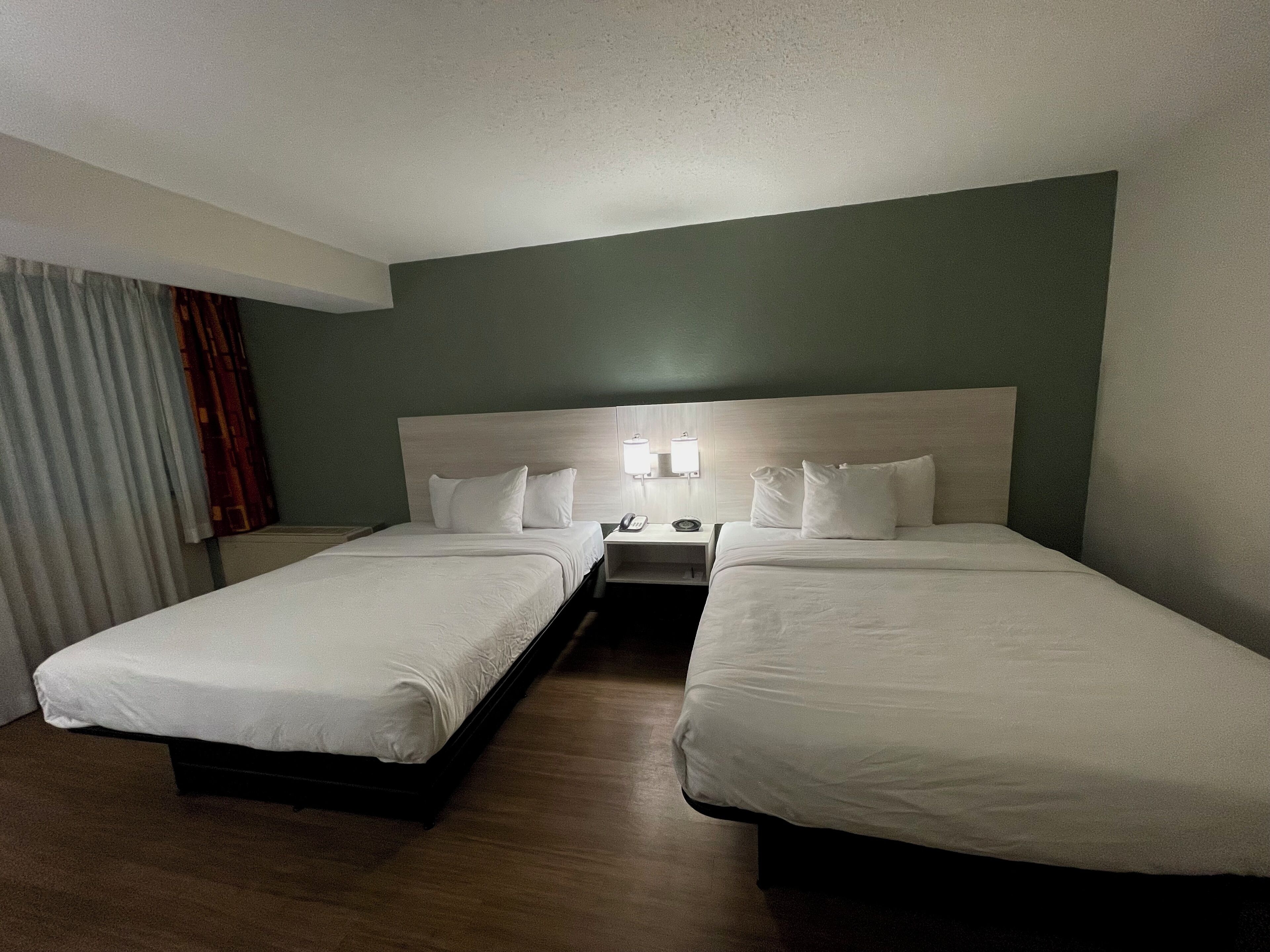 A hotel room with two single beds, a nightstand with a lamp, and a window with curtains.