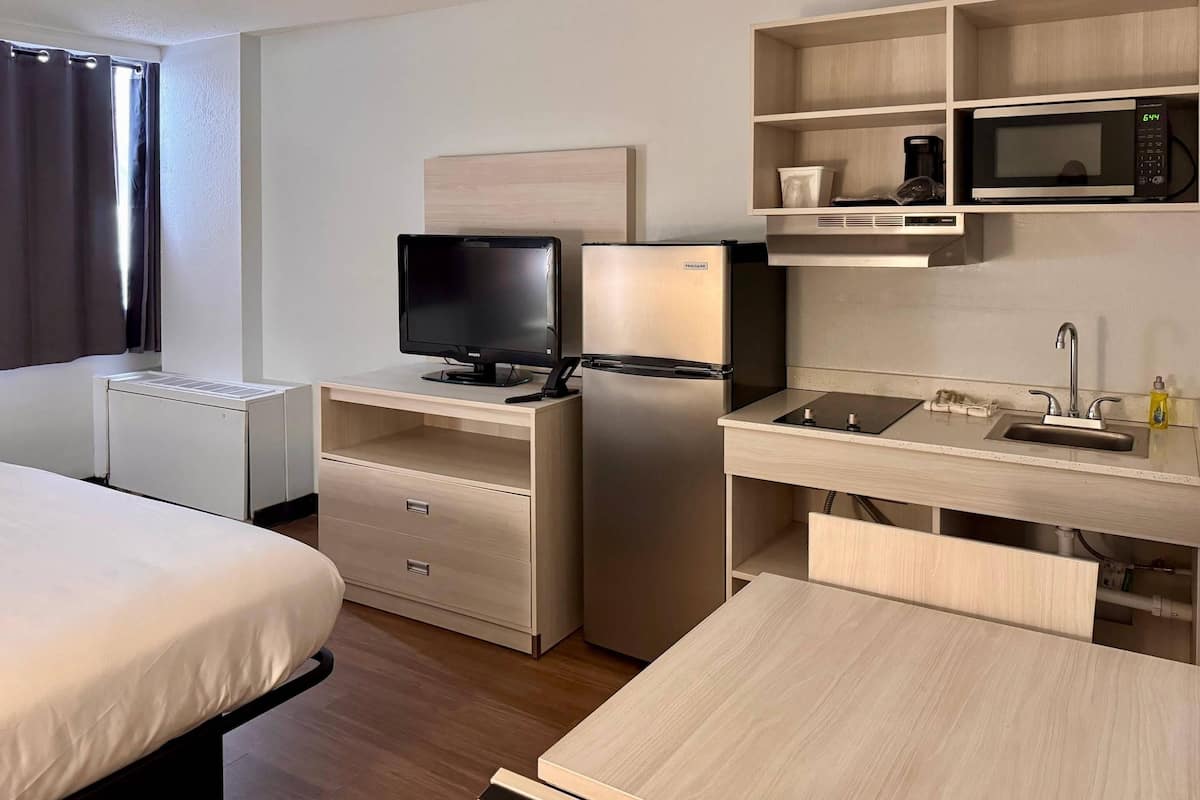 A hotel room with a bed, a desk with a computer, a refrigerator, a microwave, and a sink.