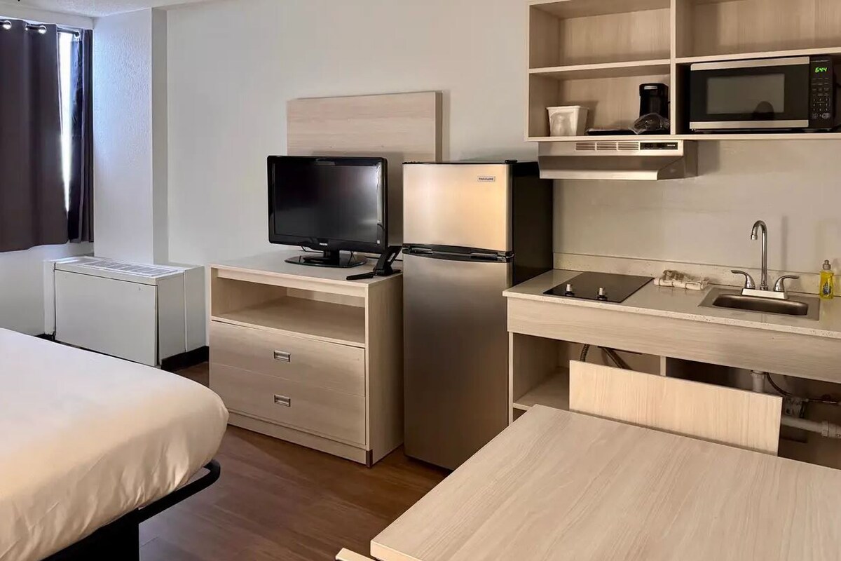 Une chambre d’hôtel compacte comprenant un lit, un bureau avec un ordinateur et un réfrigérateur, un four à micro-ondes et une petite kitchenette.