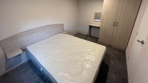 Une chambre à coucher avec un lit, une armoire en bois, un petit bureau et un miroir.