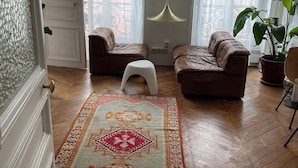 A living room with two sofas, a white stool, a patterned rug, and a hanging pendant light. - Apartment in lively neighborhood near Marais.  (Paris)