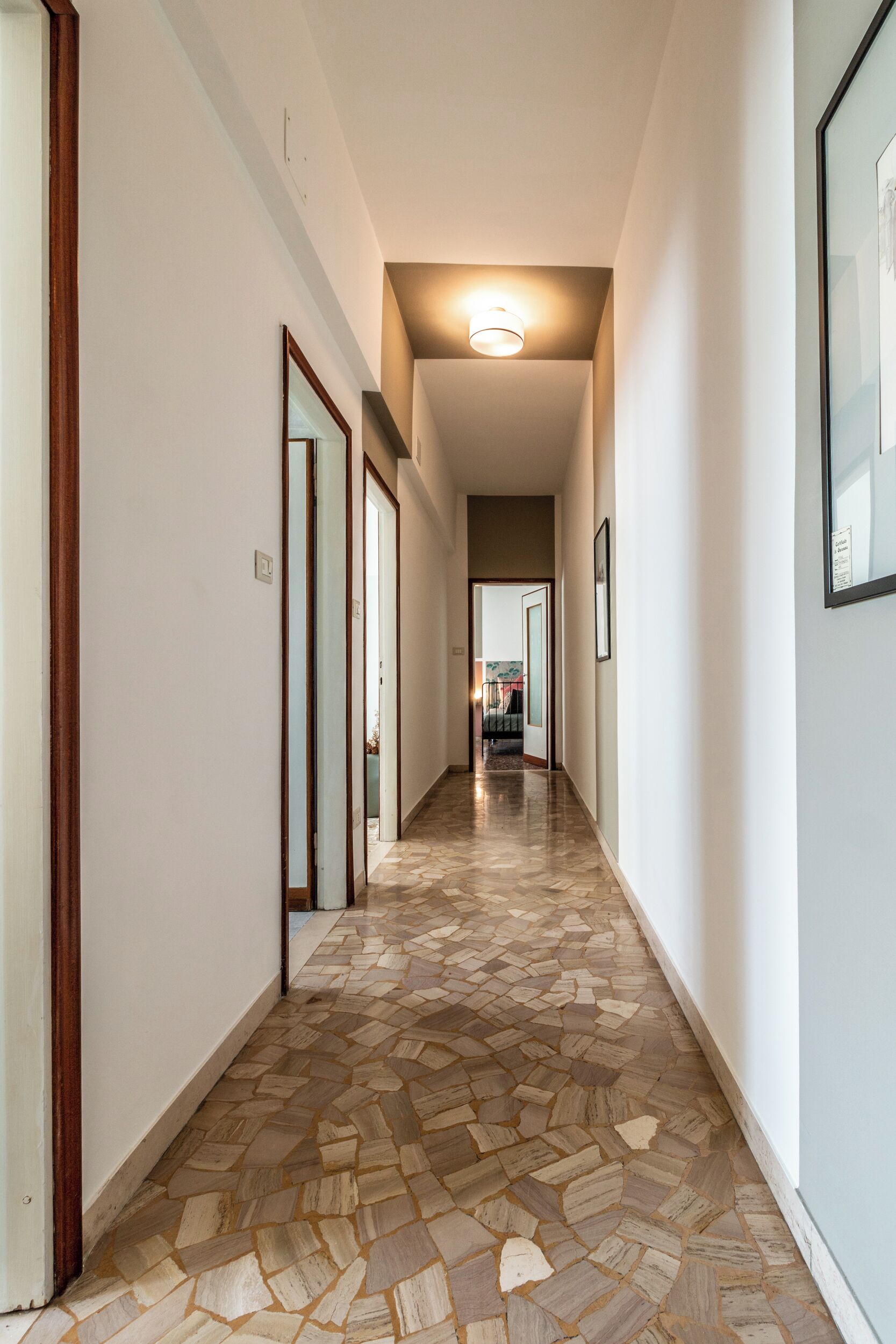 A hallway with patterned flooring, white walls, and framed pictures.