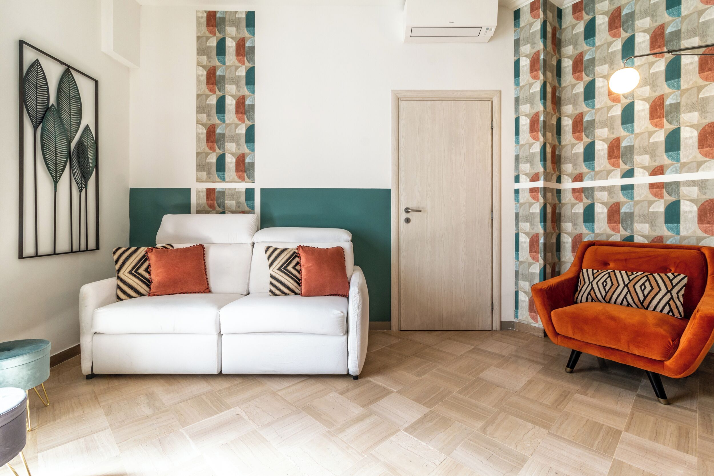 Una sala de estar moderna con un sofá blanco, un sillón naranja y papel tapiz estampado.