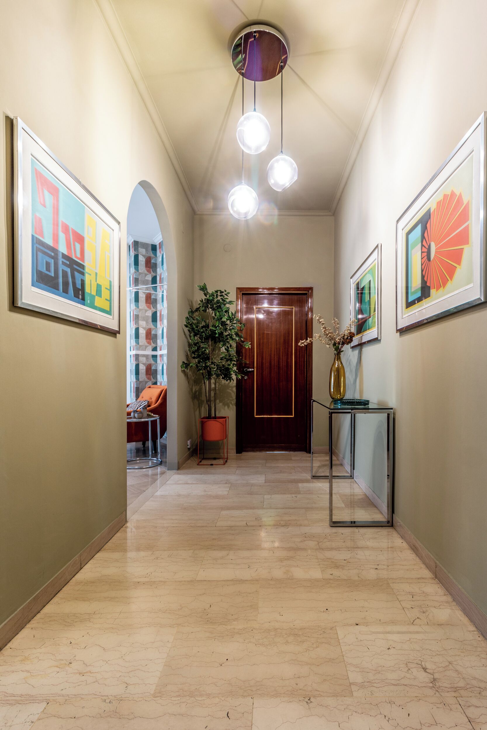 Un couloir avec une porte en bois, une plante en pot et des œuvres d’art encadrées accrochées aux murs.