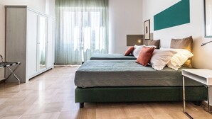 A modern bedroom with two beds, a desk, and a wardrobe.