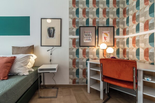 A compact room with a bed, a desk, and a chair. There are framed pictures on the wall and a patterned wallpaper. - Colorful apartment in Riva di Reno by Wonderful Italy (Bologna)