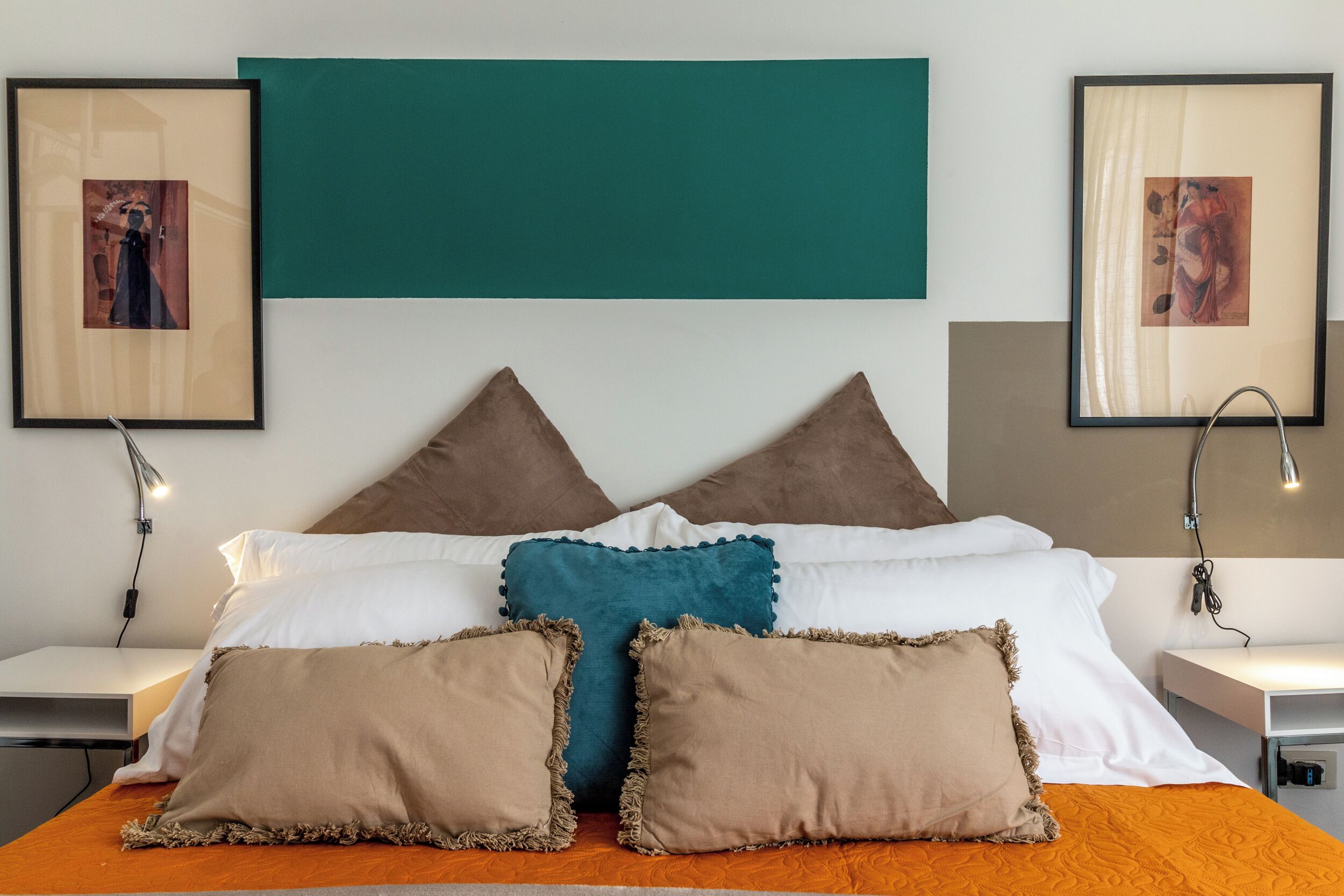 Een netjes opgemaakt slaapkamer met een bed, kussens en twee ingelijste foto’s aan de muur.