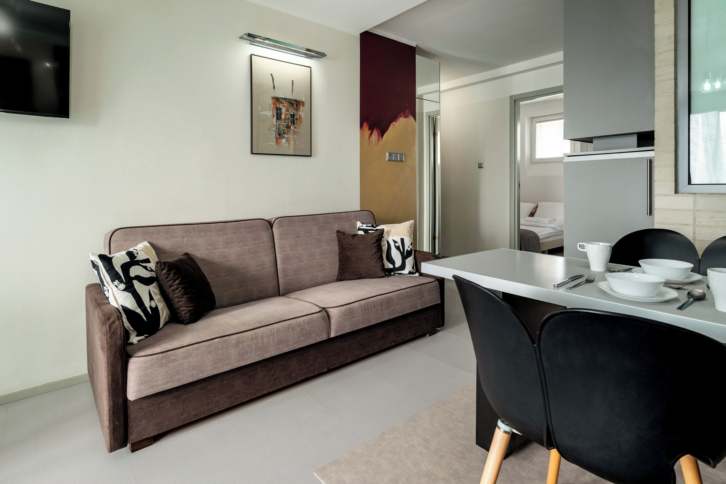 A modern living room with a sofa, a dining table with chairs, and a TV mounted on the wall.