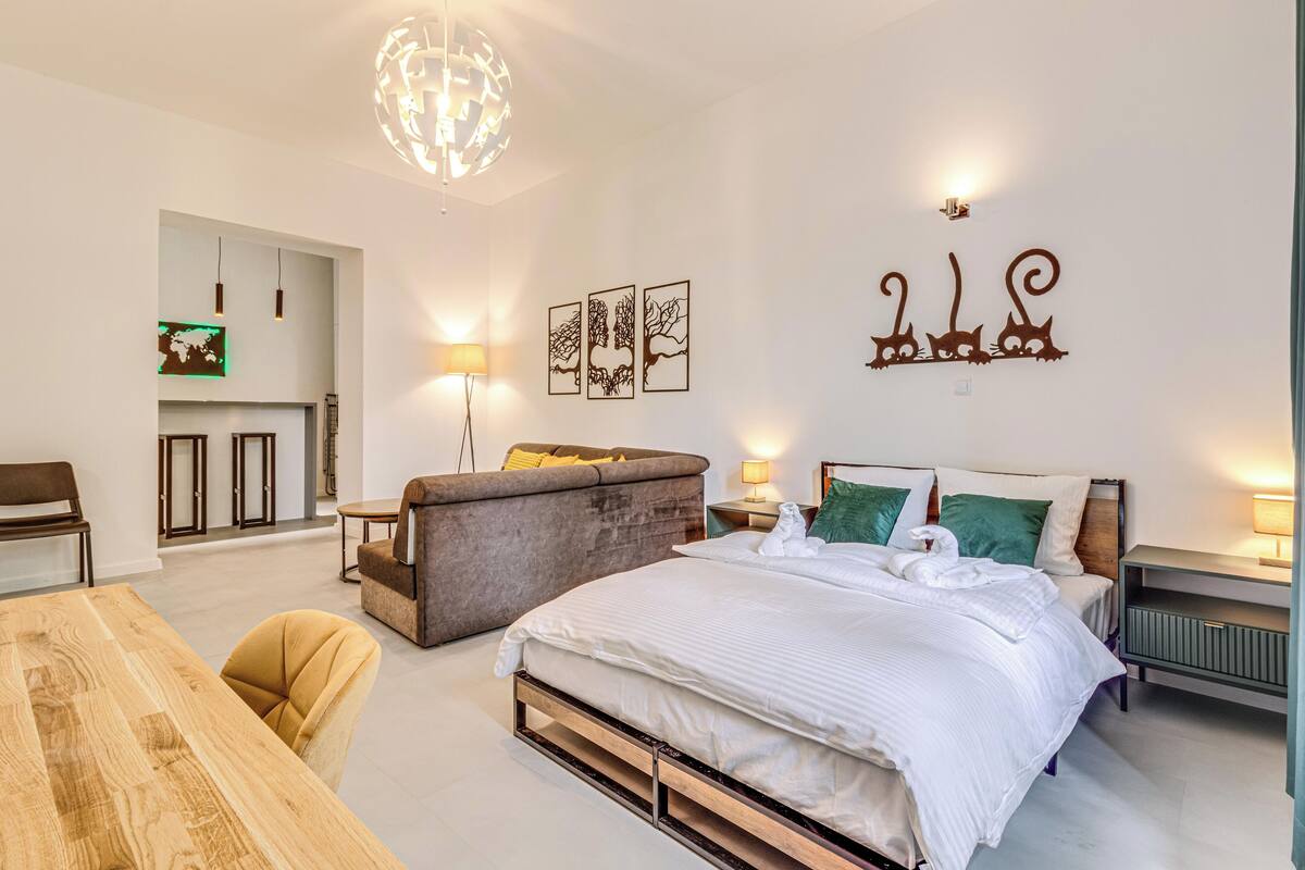 A modern bedroom with a large bed, a wooden dining table, a sofa, and a chandelier.