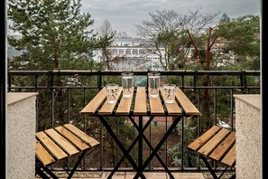 A balcony with a wooden table and chairs, overlooking a residential area with trees and a building in the background. - RentPlanet - Kazimierza Wielkiego (Wroclaw)