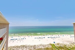 Une vue sur la plage depuis un balcon, avec un ciel dégagé, une plage de sable et l’océan.