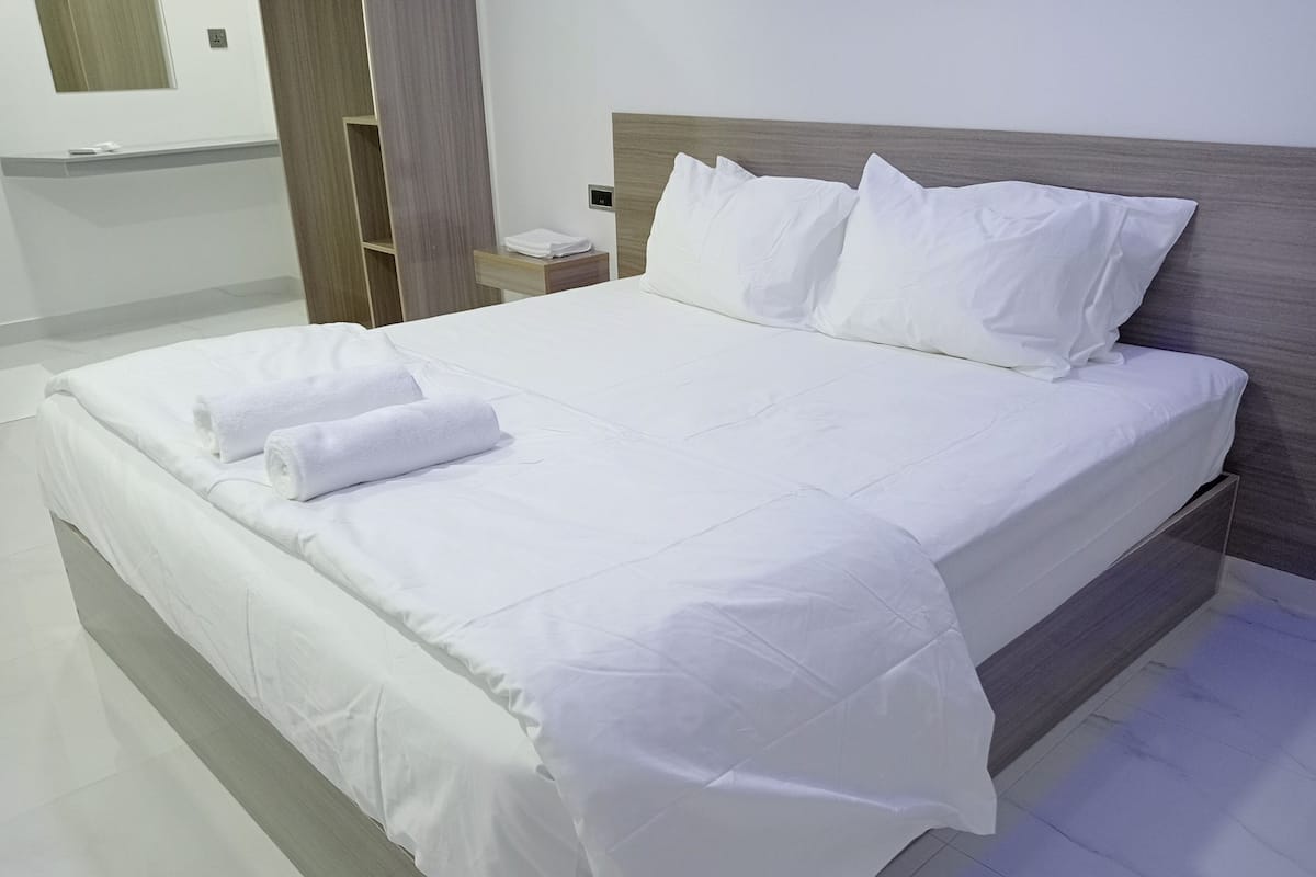 A neatly made bed with white linens, a wooden headboard, and a small bedside table with a lamp.