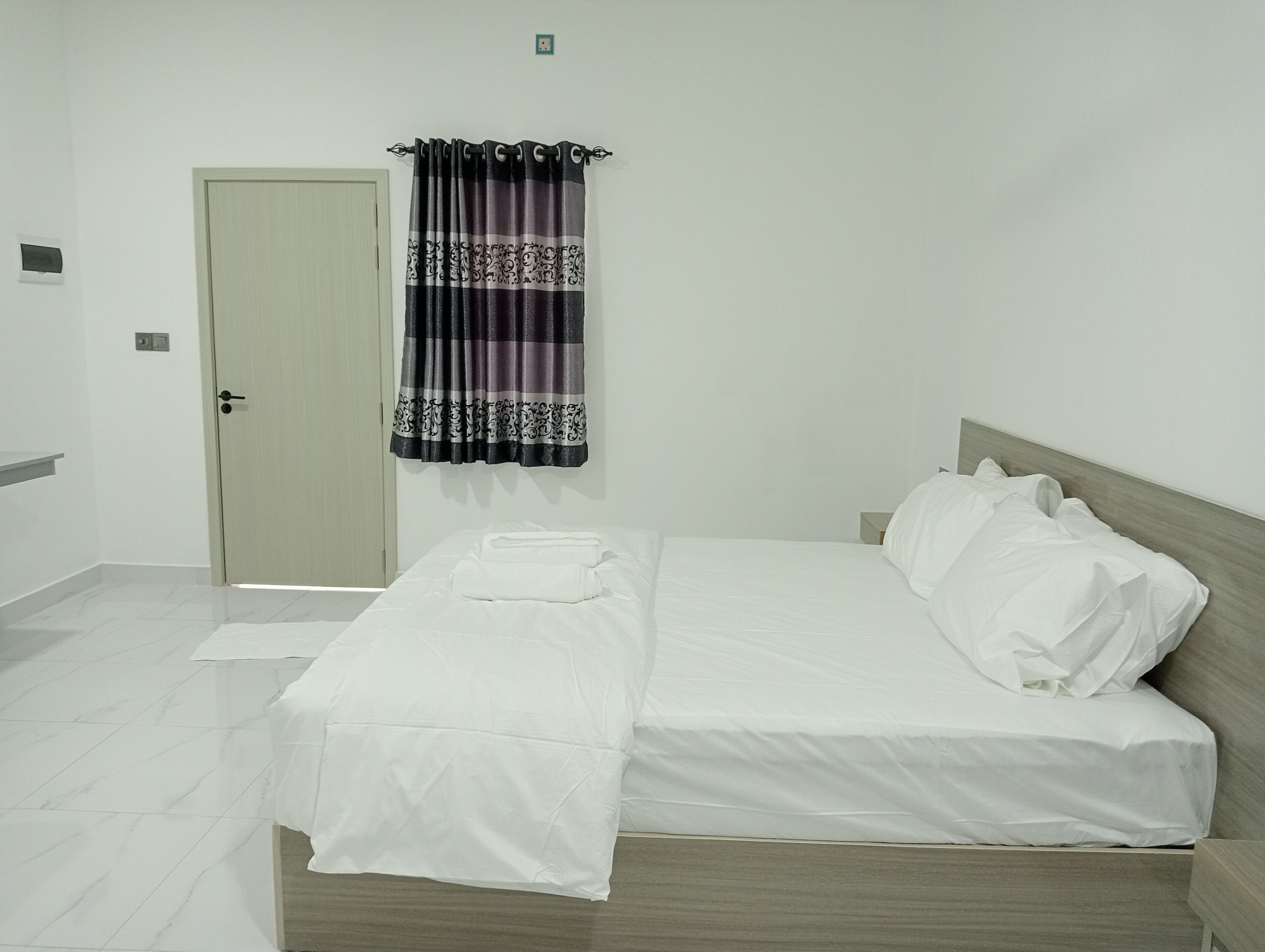 Una cama bien hecha con sábanas blancas, un cabecero de madera y una puerta con interruptor de luz en la pared.