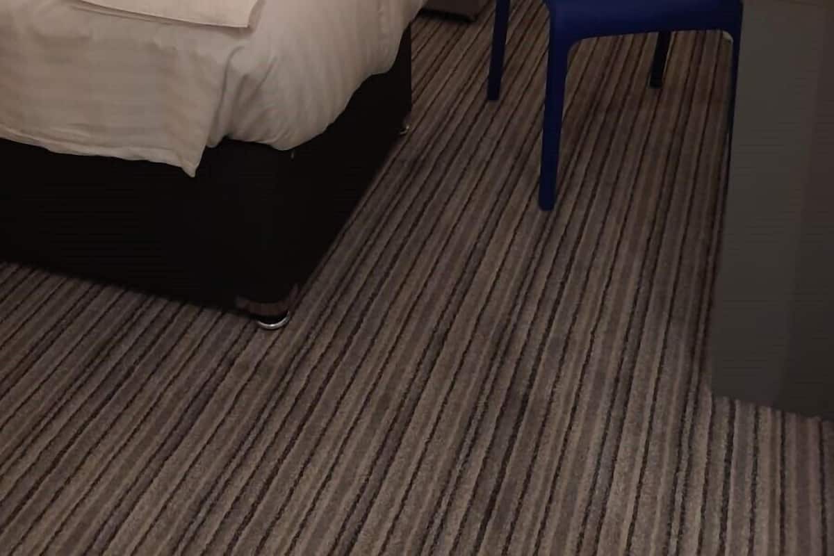 Une chambre d’hôtel avec trois lits, une chaise bleue et un bureau avec une tasse.