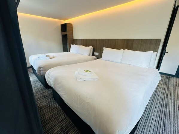 Een hotelkamer met twee bedden, elk voorzien van witte lakens en handdoeken, een houten hoofdbord en een tapijtvloer.