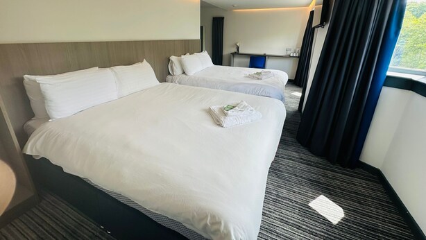 A hotel room with two beds, a desk, a chair, and a window with curtains. - My Motel (Paisley)