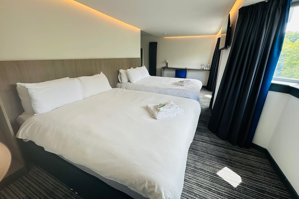 Une chambre d’hôtel avec deux lits, un bureau, une chaise et une fenêtre avec des rideaux.