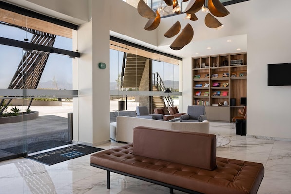 Een modern interieur met een leren bank, een trap, een boekenkast en een groot raam met uitzicht op de omgeving.