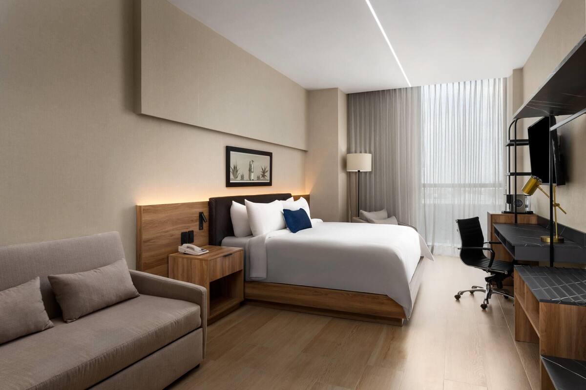 A modern hotel room with a bed, a sofa, a desk, and a TV.