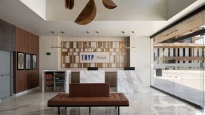 Um lobby moderno com balcão de recepção, área de estar e uma grande janela com vista para a rua.