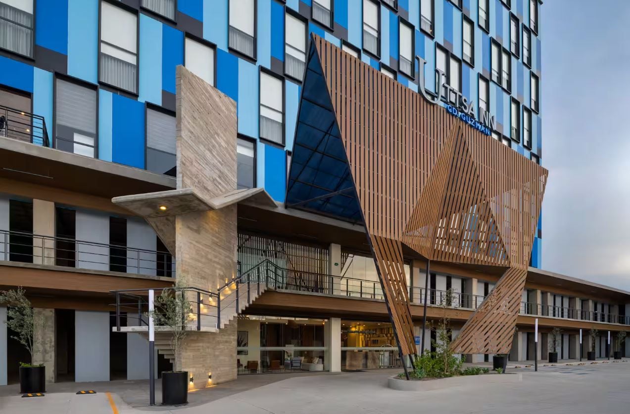 Un hotel moderno con una fachada distintiva que presenta paneles azules y marrones, una estructura de madera a listones muy visible y una entrada con escaleras.