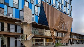 Un hotel moderno con una fachada distintiva que presenta paneles azules y marrones, una estructura de madera a listones muy visible y una entrada con escaleras.